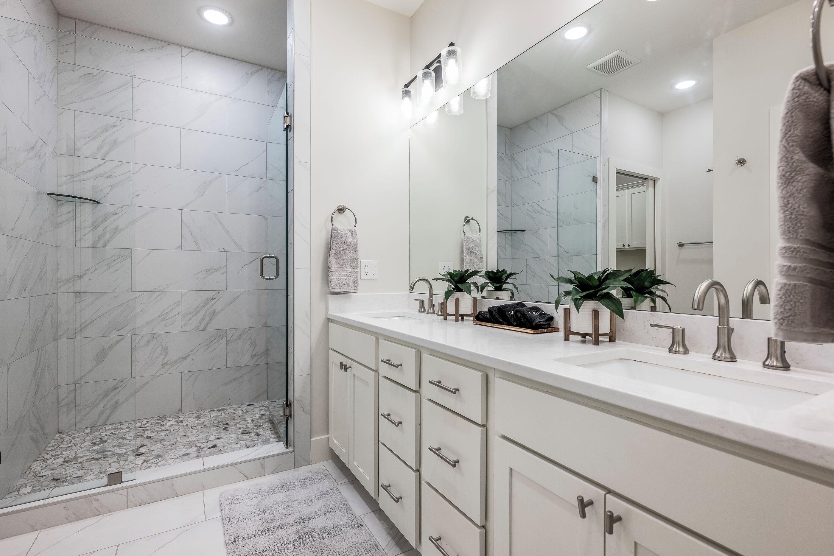 A modern bathroom with a walk-in shower, a large mirror, and a white vanity with drawers.