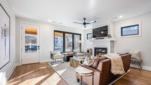 Un salon moderne doté d’une cheminée, d’un ventilateur de plafond et d’une grande fenêtre.