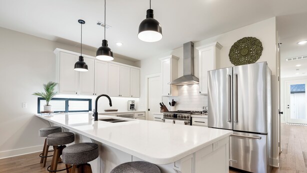Une cuisine moderne dotée d’un îlot central, d’appareils électroménagers en acier inoxydable et de luminaires suspendus.