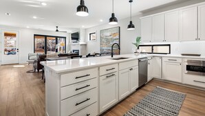 Une cuisine moderne avec des meubles blancs, un îlot central, des luminaires suspendus et une vue sur la salle à manger.