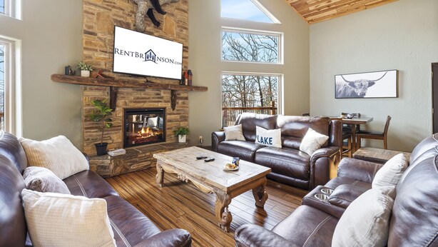 A spacious living room with a stone fireplace, leather sofas, a wooden coffee table, and a mounted TV. - Scenic Table Rock Shoreline w/ Access, Free Daily Tickets & Shared Amenities (Branson)