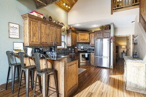 A kitchen with wooden cabinets, stainless steel appliances, and a bar area with stools. - Scenic Table Rock Shoreline w/ Access, Free Daily Tickets & Shared Amenities (Branson)