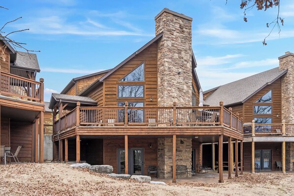 A large, multi-story log cabin with a stone chimney, wooden balconies, and a covered patio area.