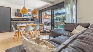 A modern living room with a grey sofa, a dining area with white chairs, and a kitchen with a black countertop. - Beautiful home in Fazana (Fazana)