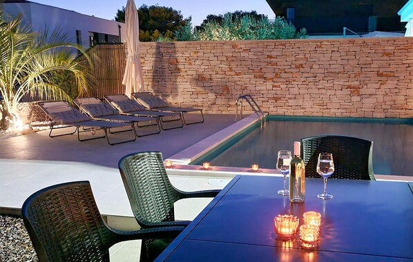 A poolside area with lounge chairs, a table with candles, and a bottle of wine. - Beautiful home in Fazana (Fazana)