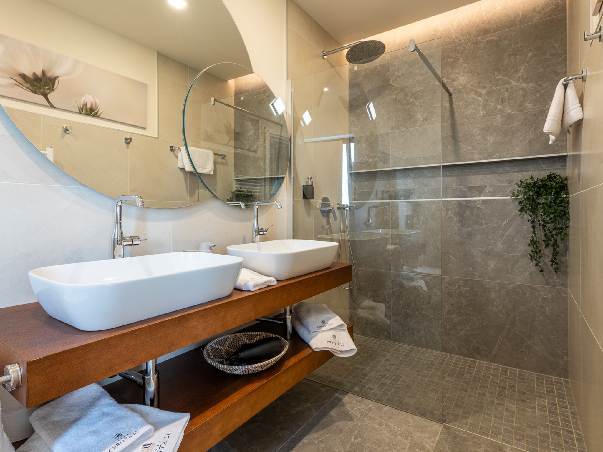 A modern bathroom with two sinks, a glass shower enclosure, and a wooden vanity.