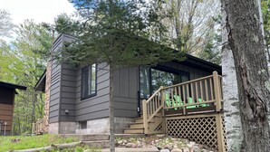 A two-story cabin with a wooden deck and a stone foundation. - Cozy cottage on Bearskin Lake! (Harshaw)