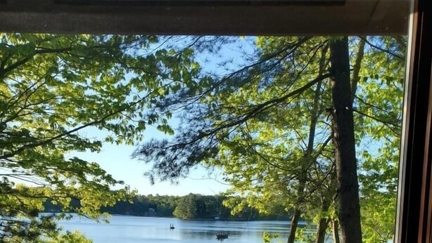 A lakeside view from a covered deck with a railing, a flag, and a boat in the water. - Cozy cottage on Bearskin Lake! (Harshaw)