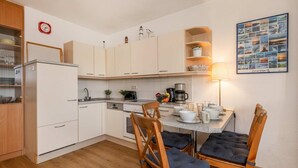 Cocina compacta con alacenas blancas, una mesa de comedor con sillas, una cafetera y una lámpara de pared.