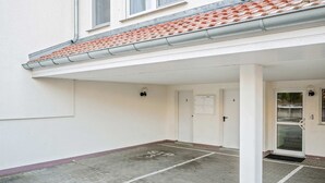 Entrada de un edificio con zona cubierta, puertas numeradas y espacio exterior visible.