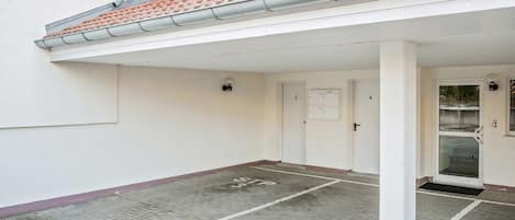 Entrada de un edificio con zona cubierta, puertas numeradas y espacio exterior visible.