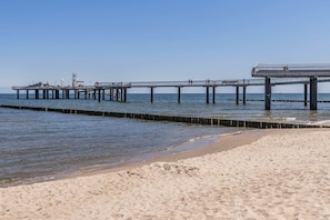 A beach with a pier extending into the water, featuring a walkway and several people walking. - Ferienwohnung Schrabbe - Ferienwohnung Schrabbe in Koserow (Koserow)
