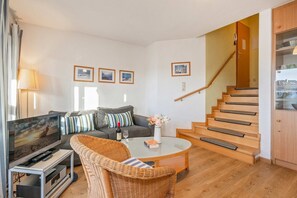 A living room with a sofa, a television, a coffee table, and a wicker chair. There is a staircase leading to an upper floor. - Ferienwohnung Schrabbe - Ferienwohnung Schrabbe in Koserow (Koserow)