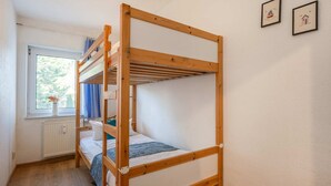 Una cama individual superpuesta en una habitación con ventana, radiador y dos cuadros en la pared.