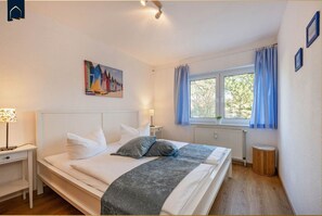 A bedroom with a bed, bedside tables, a window with curtains, a radiator, and a painting on the wall.