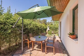 Eine Terrasse im Freien mit Tisch und Stühlen, einem grünen Sonnenschirm und einem Backofen aus Ziegeln.