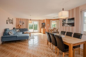 Ein Wohnzimmer mit blauem Sofa, einem Esstisch mit Stühlen und einer Küche im Hintergrund.