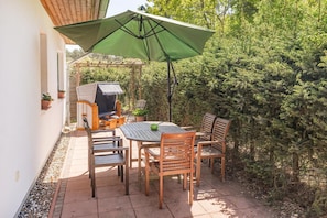 Une terrasse extérieure avec une table, des chaises, un barbecue et un parasol vert.