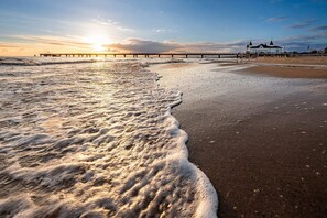 Ein Strand mit Wellen, einem Steg und einem Gebäude mit spitzem Dach.