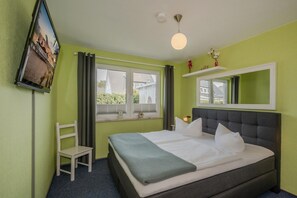 Ein Schlafzimmer mit einem Bett, einem Sessel, einem Fenster, einem Spiegel und einer Deckenleuchte.