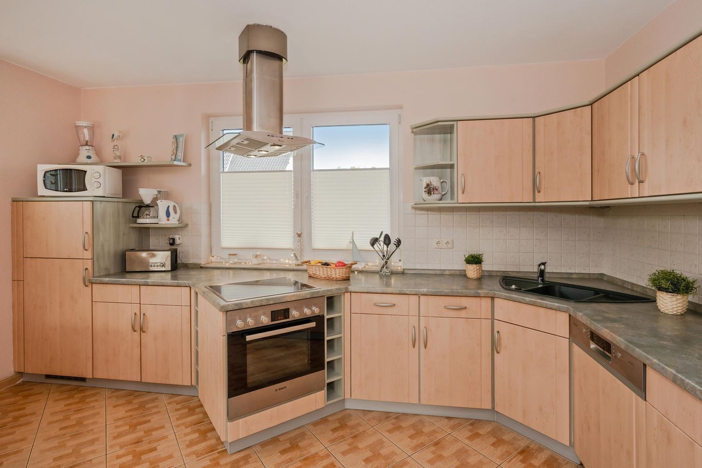 Une cuisine moderne avec des meubles en bois, un four encastré, un four à micro-ondes et une fenêtre avec des stores.