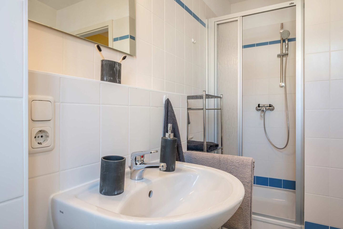 A bathroom with a white sink, a mirror, a towel rack, and a shower.