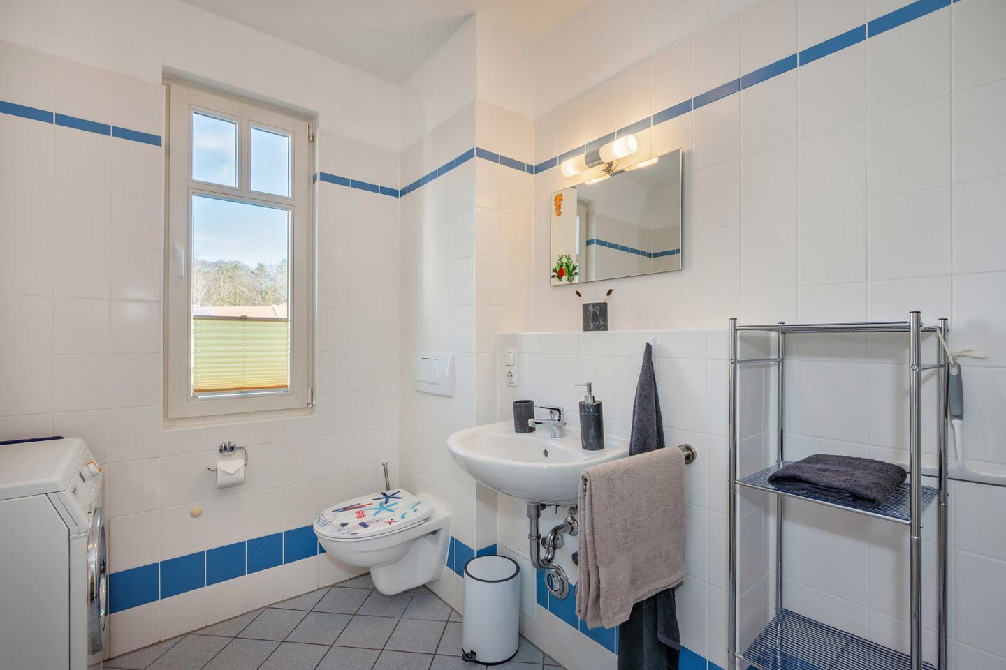 Une salle de bain comprenant des toilettes, un lavabo, un miroir, un porte-serviettes et une fenêtre.