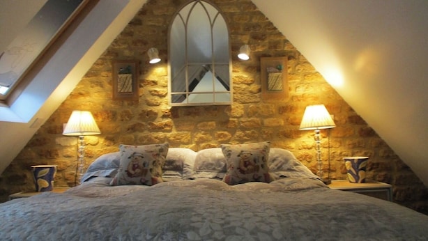 A bedroom with a stone wall, a skylight, and a bed with floral pillows. - Wonderful Picturesque Countryside Cottage (Broughton)