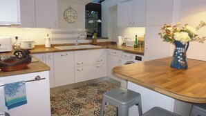 A kitchen with white cabinets, a wooden countertop, a sink, a clock, and a vase with flowers. - Wonderful Picturesque Countryside Cottage (Broughton)