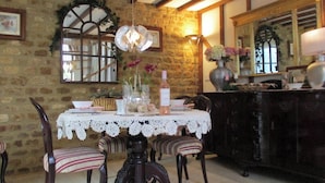 A dining area with a stone wall, wooden beams, a lace tablecloth, striped chairs, a chandelier, and a mirror. - Wonderful Picturesque Countryside Cottage (Broughton)