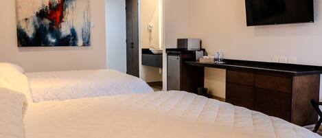 A hotel room with two beds, a flat-screen TV, a painting, and a kitchenette.