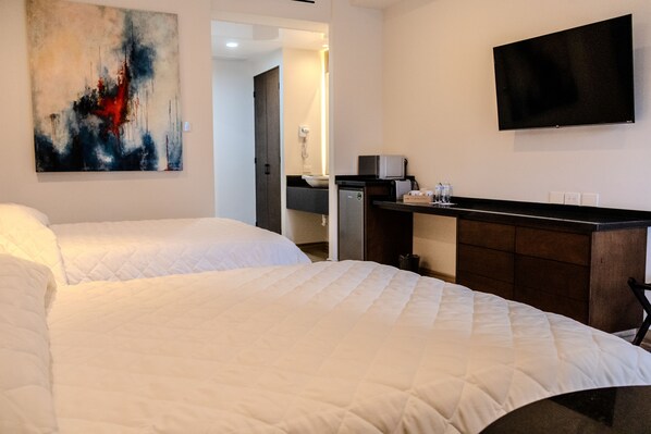 Habitación de hotel con dos camas, un televisor de pantalla plana, un cuadro y una kitchenette.