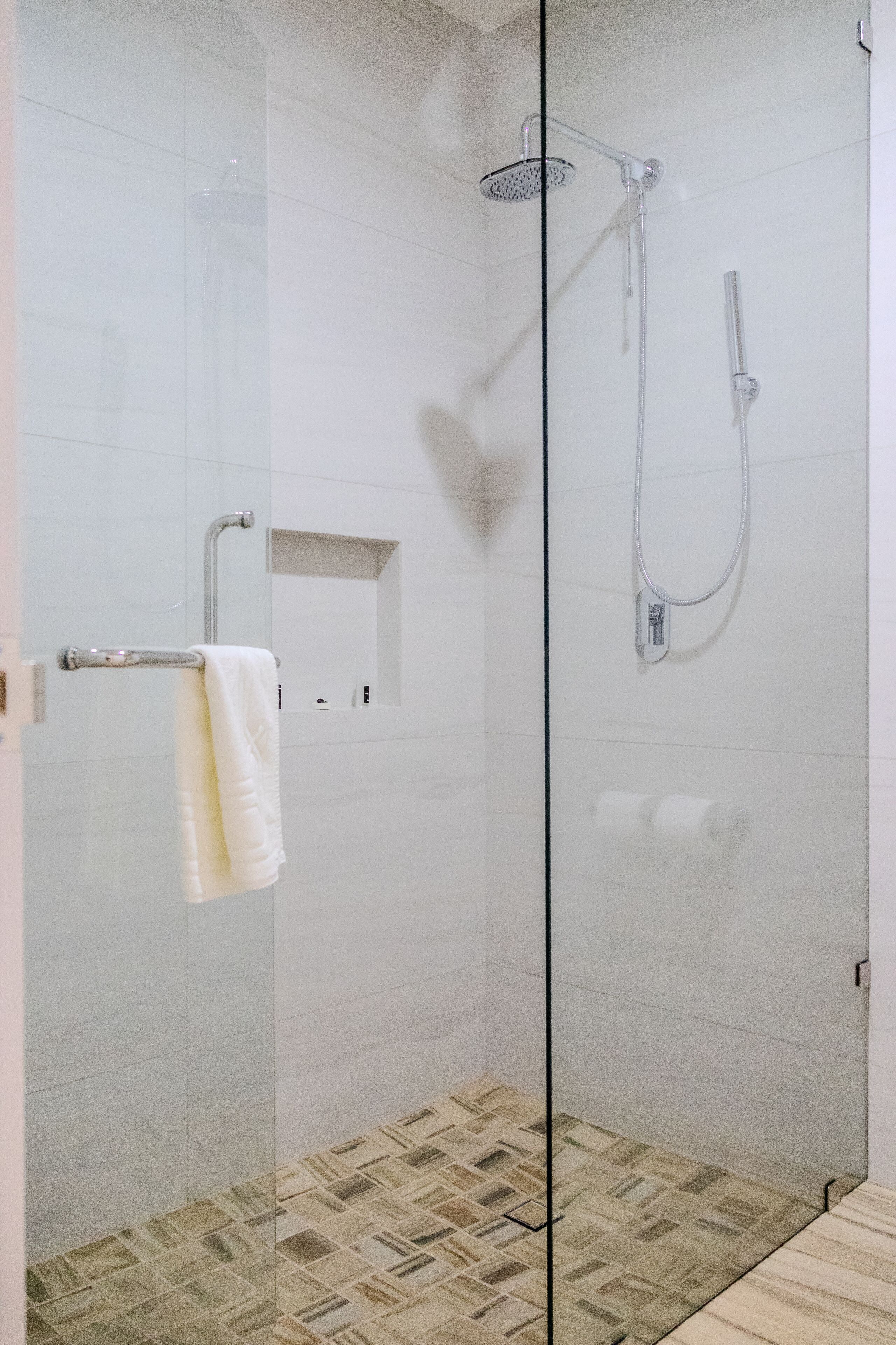Ducha con cerramiento de vidrio, cabezal de ducha manual y grifo empotrado.