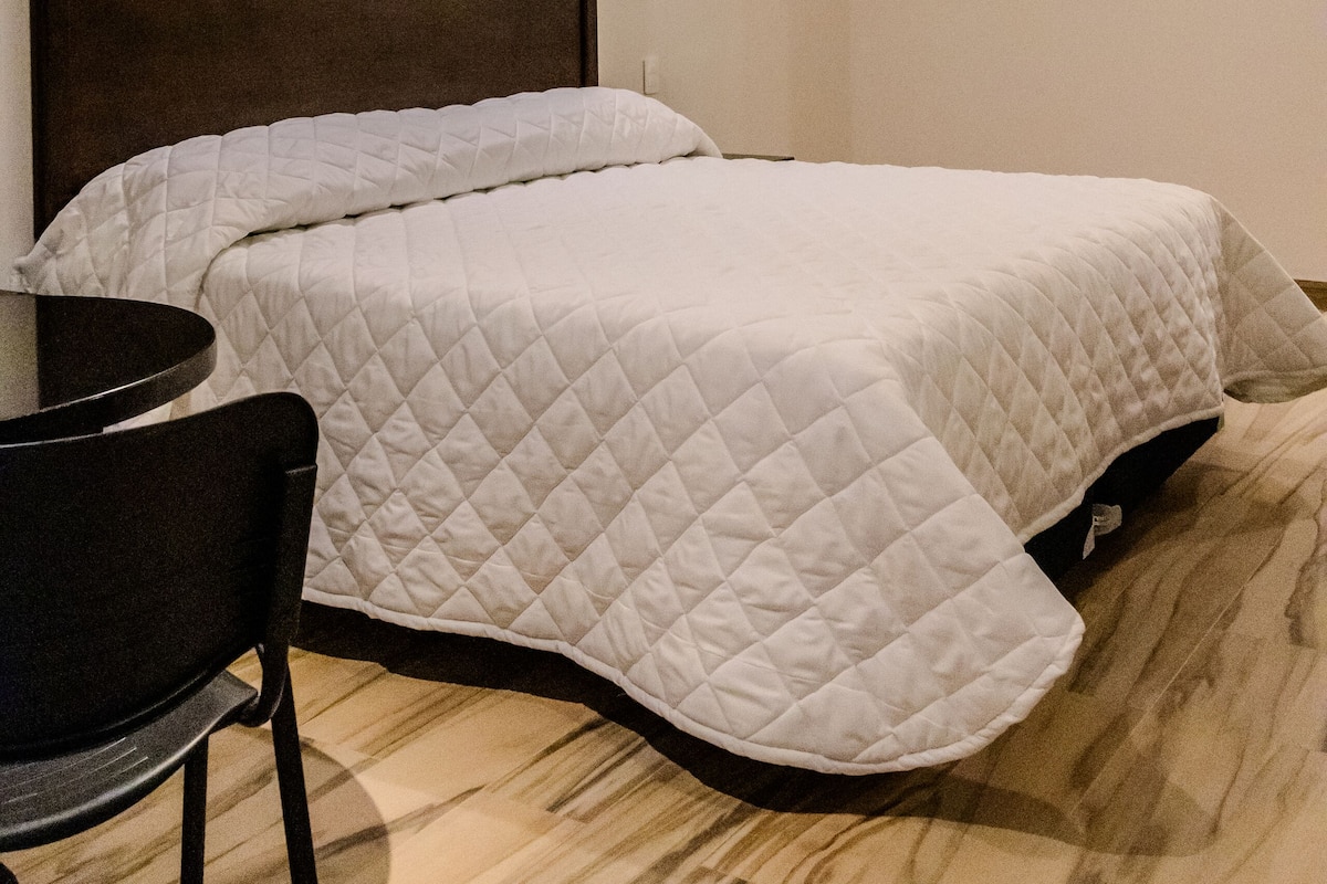 Un dormitori amb llit, una cadira, una taula i un ventilador de sostre.