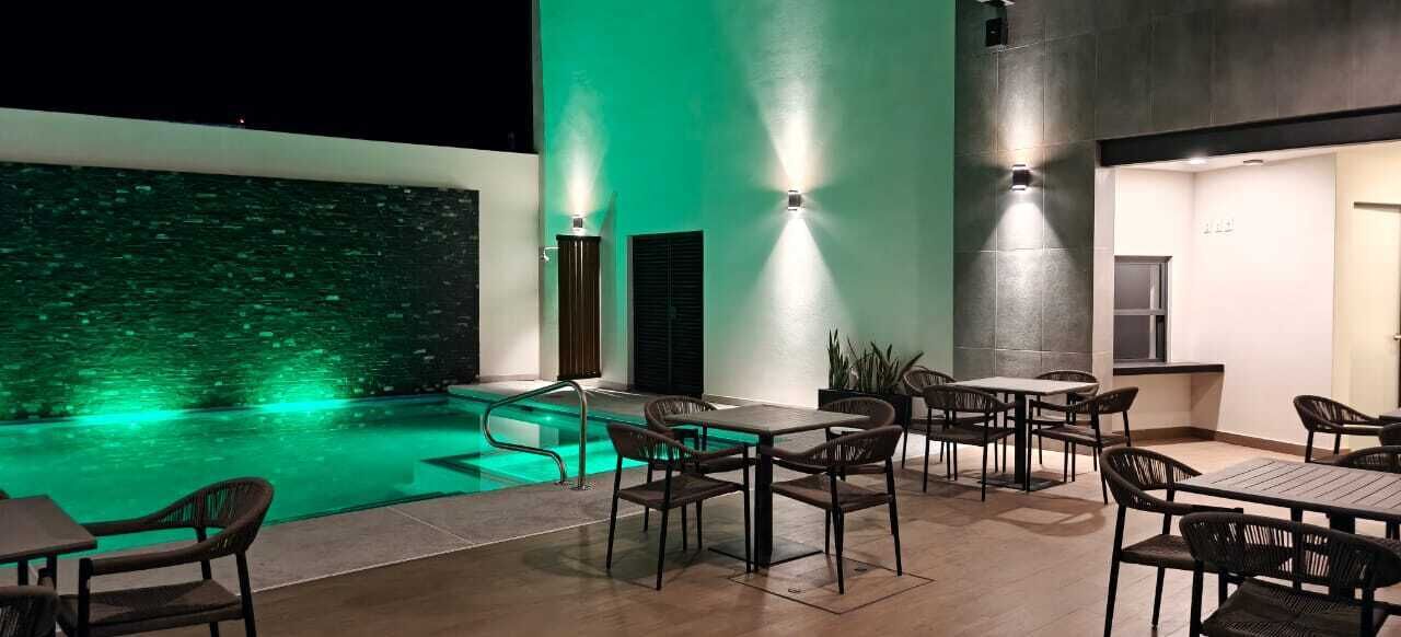 An outdoor pool area with seating and tables, surrounded by walls with light fixtures.