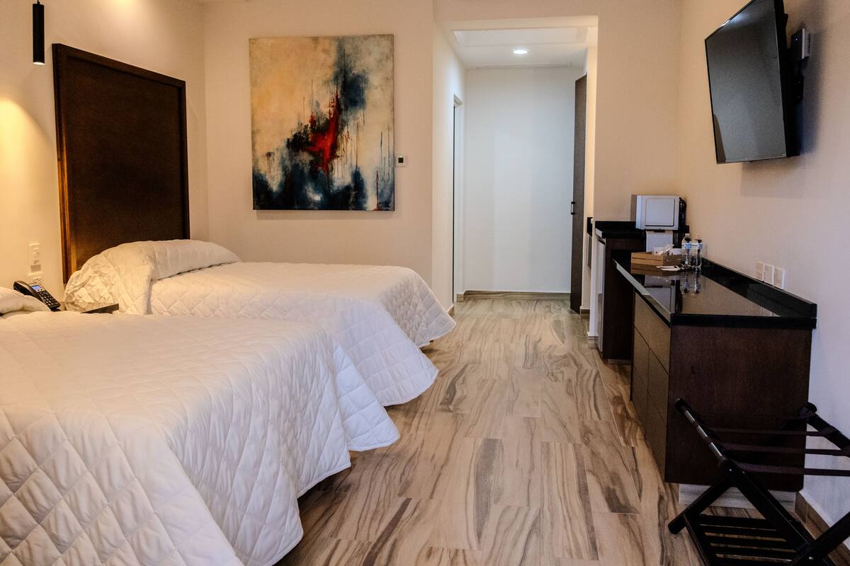 Habitació d'hotel amb dos llits, una taula de treball, un televisor i un quadre a la paret.