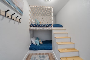 Ein kleines Zimmer mit einem Etagenbett, einer Holztreppe und einem an der Wand befestigten Kleiderhaken.