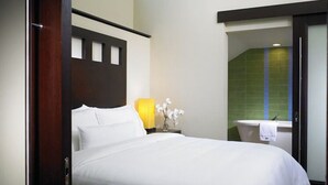 A hotel room with a bed, a nightstand with a lamp, a vase with flowers, and a view of the bathroom. - Beautiful St John Westin Villa - 2 bedroom Bay Vista (Cruz Bay)