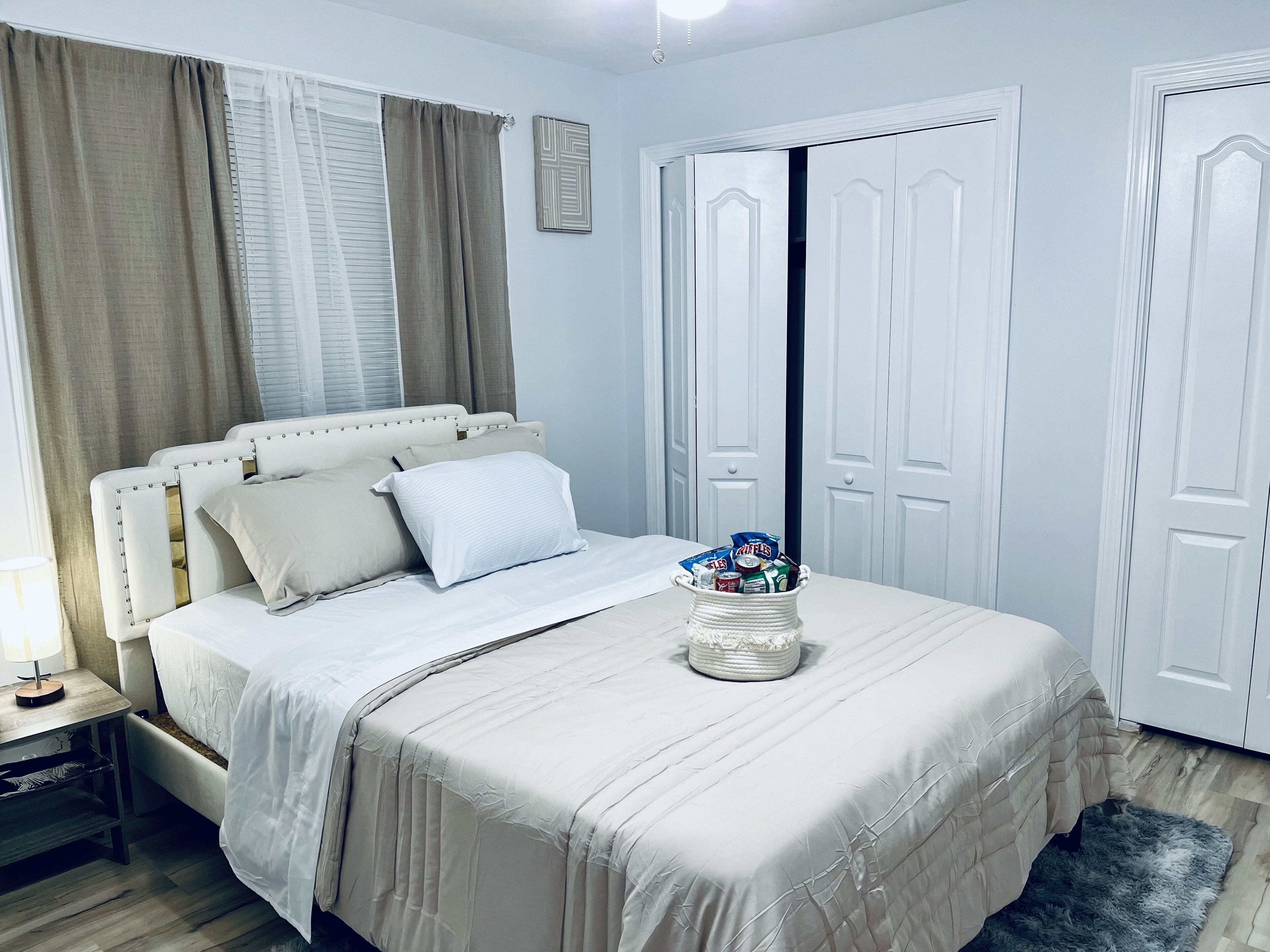 A neatly arranged bedroom with a bed, bedside table, and a basket of toiletries.