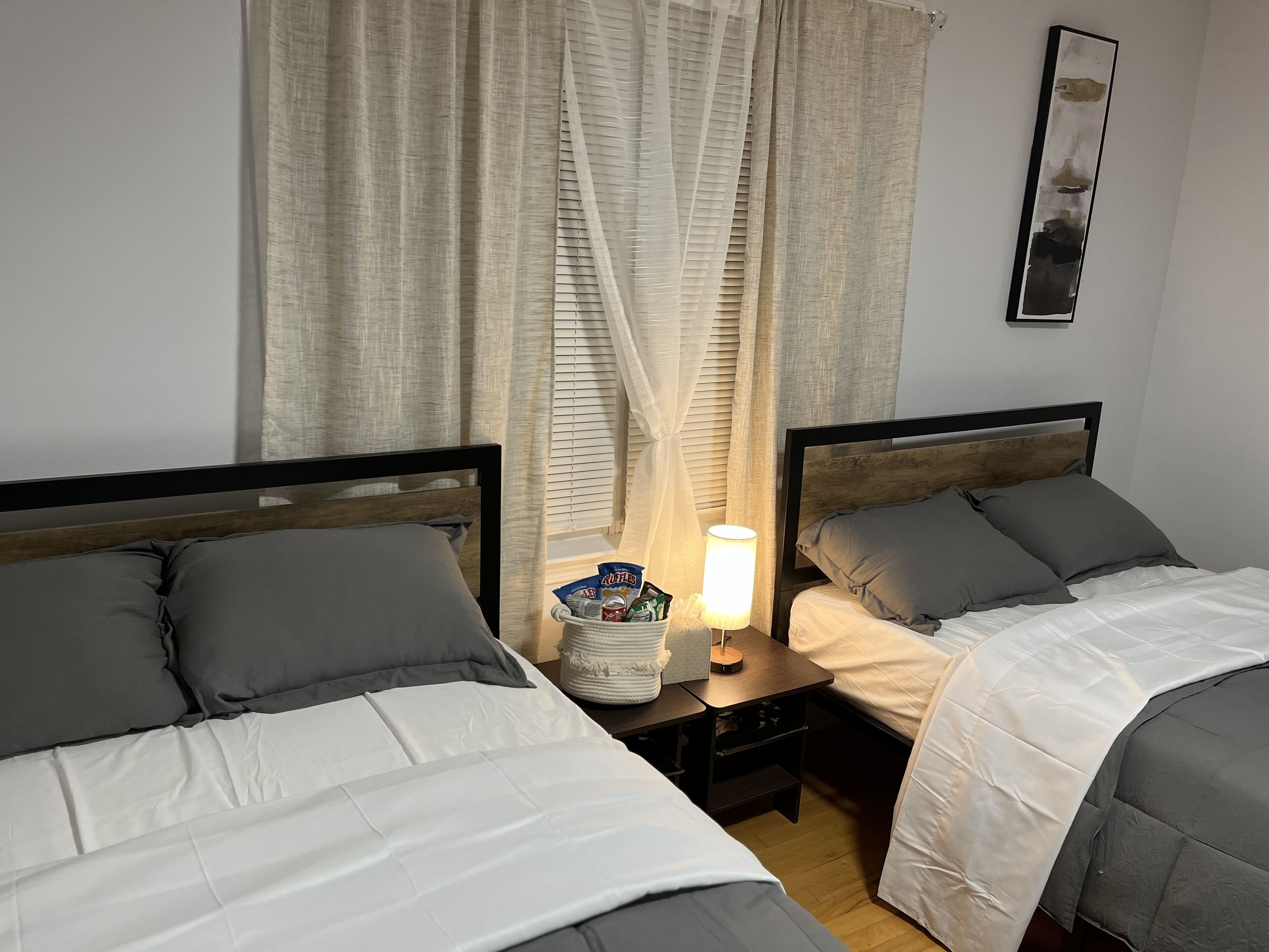 Et hotelværelse med to senge, et natbord med lampe og et vindue med gardiner.