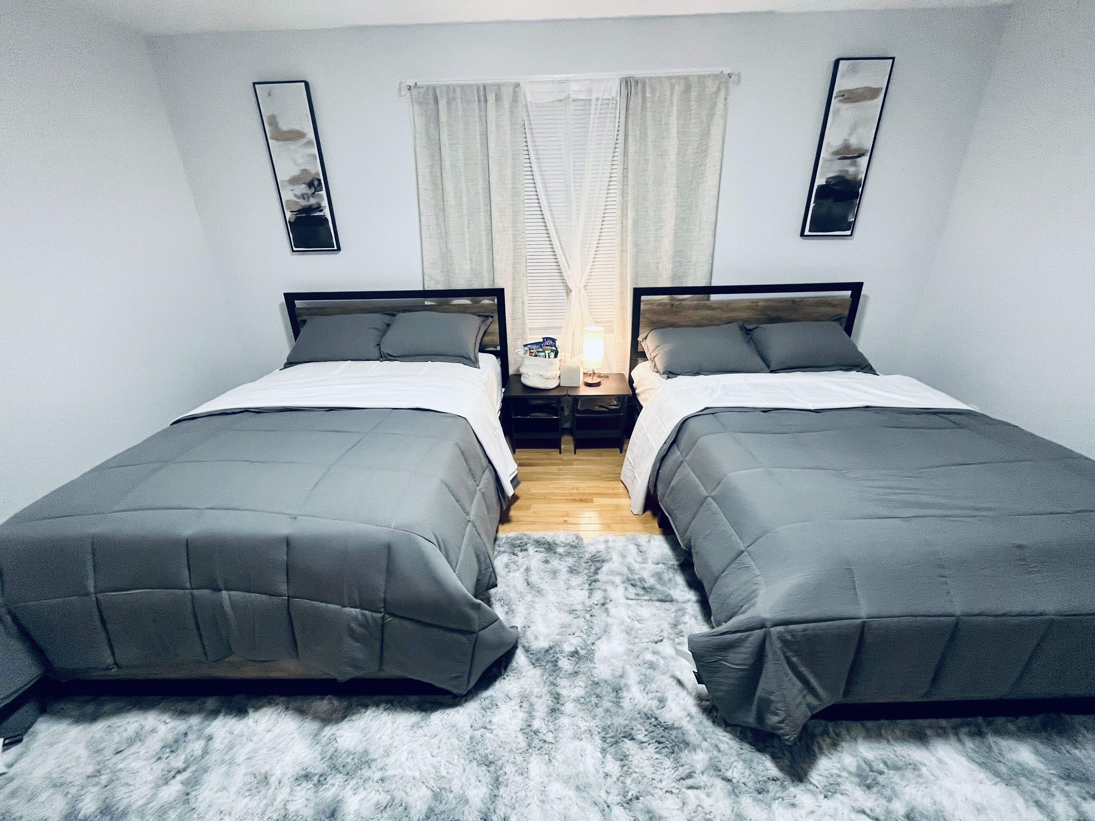 A room with two single beds, a nightstand, a lamp, and a window with curtains.