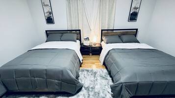 A room with two single beds, a nightstand, a lamp, and a window with curtains.