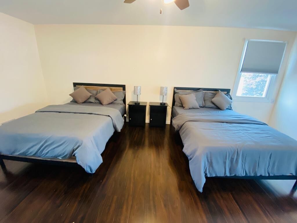 A bedroom with two single beds, wooden flooring, bedside tables with lamps, and a window with a view.