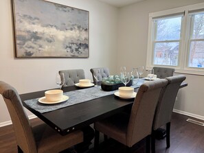 A dining table with chairs, a painting, and a window with a view.