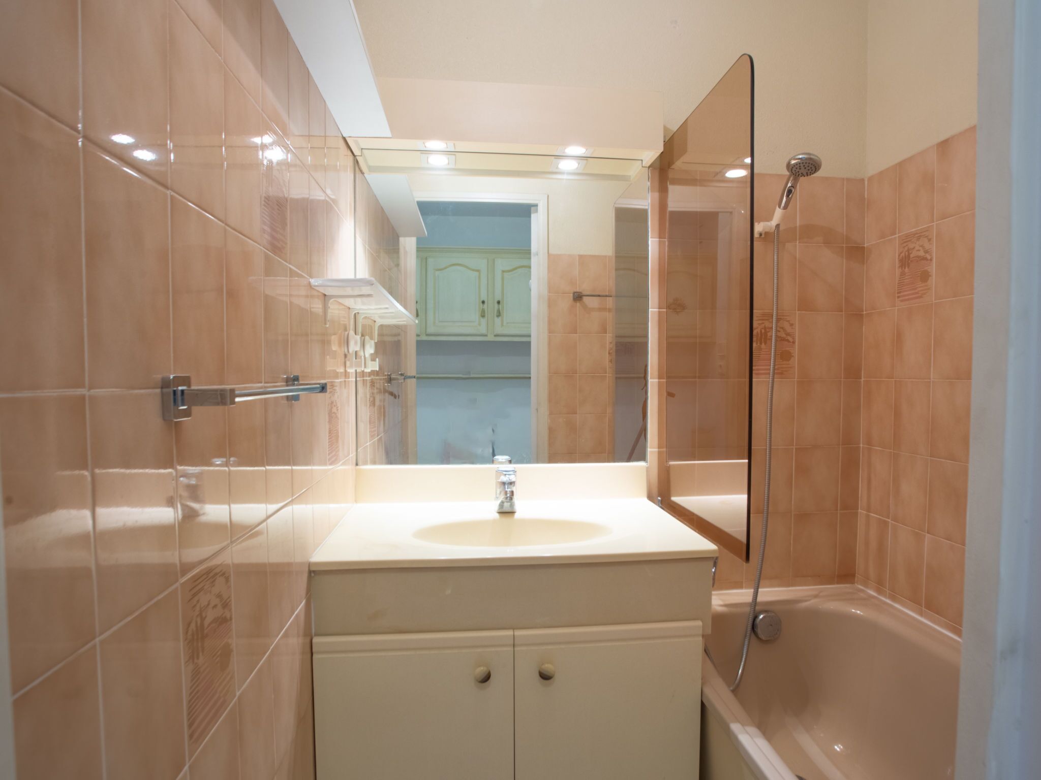 Et moderne badeværelse med en glasbrusekabine, en vask med spejl og beige klinkevægge.
