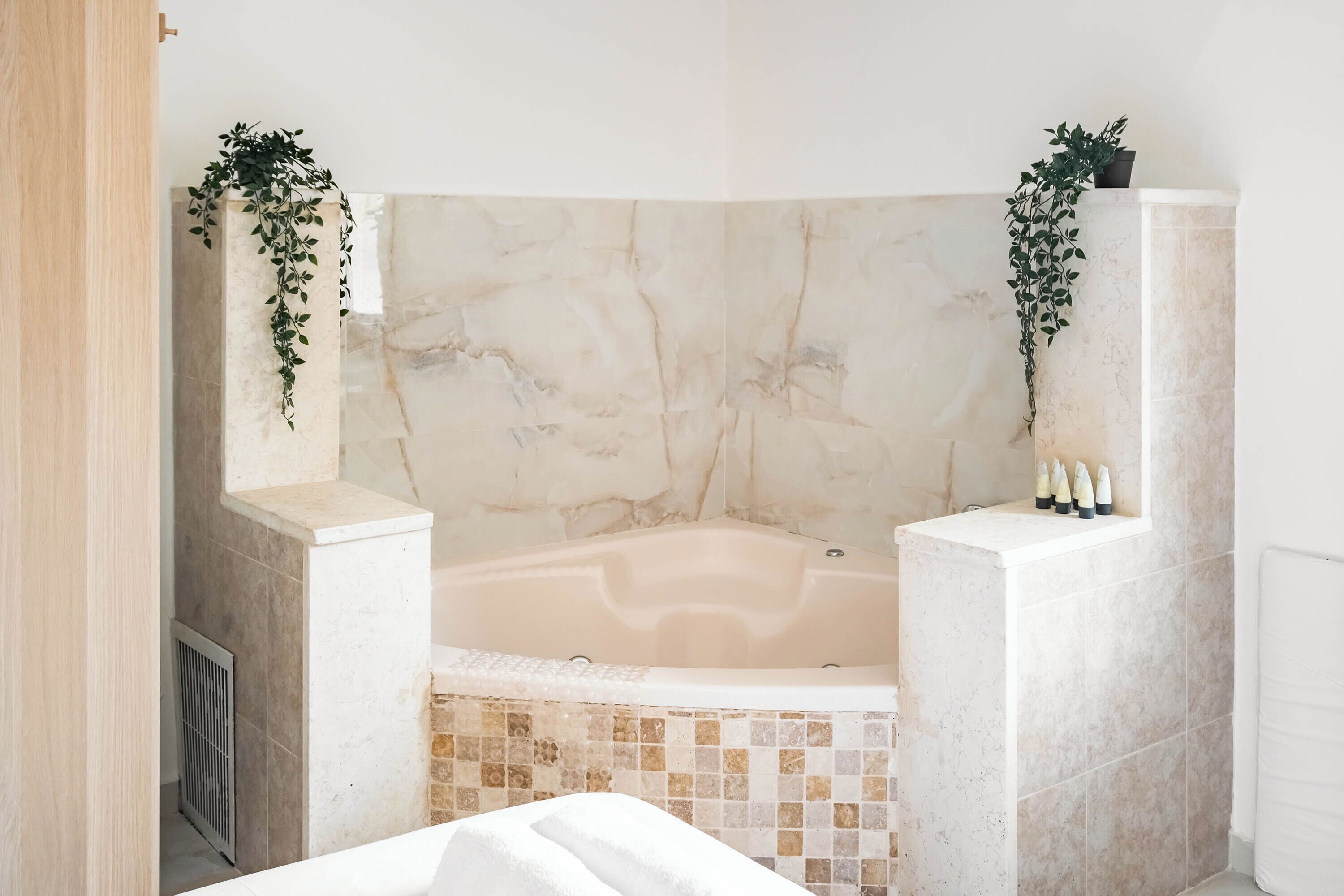 A bathroom with a marble bathtub, a tiled shower area, and two potted plants.