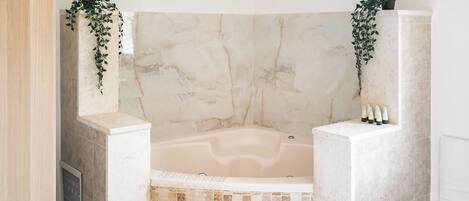 A bathroom with a marble bathtub, a tiled shower area, and two potted plants.