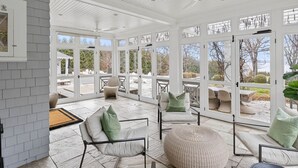 A sunroom with large glass doors, wicker furniture, and a tiled floor.