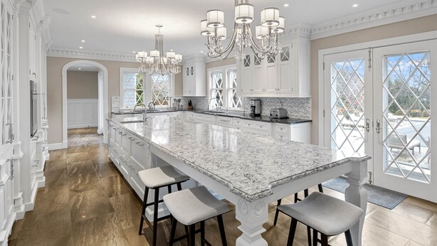 A spacious kitchen with a large island, white cabinetry, and a chandelier.