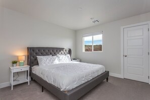Un dormitorio con cama, mesita de noche, ventana con vistas y puerta.